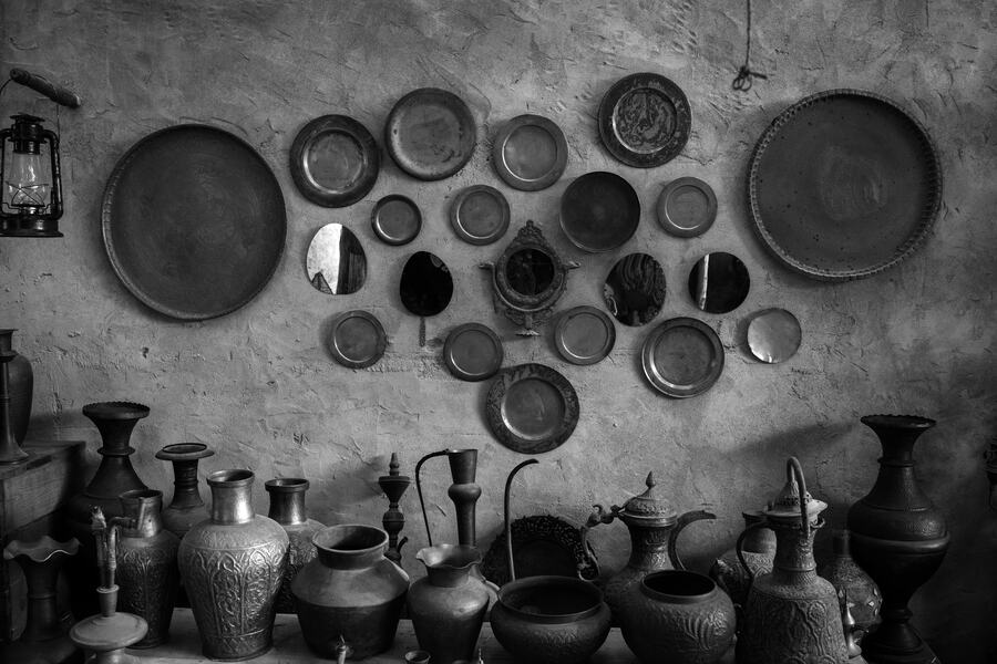 A wall of vintage plates and metal vessels, photographed in black and white